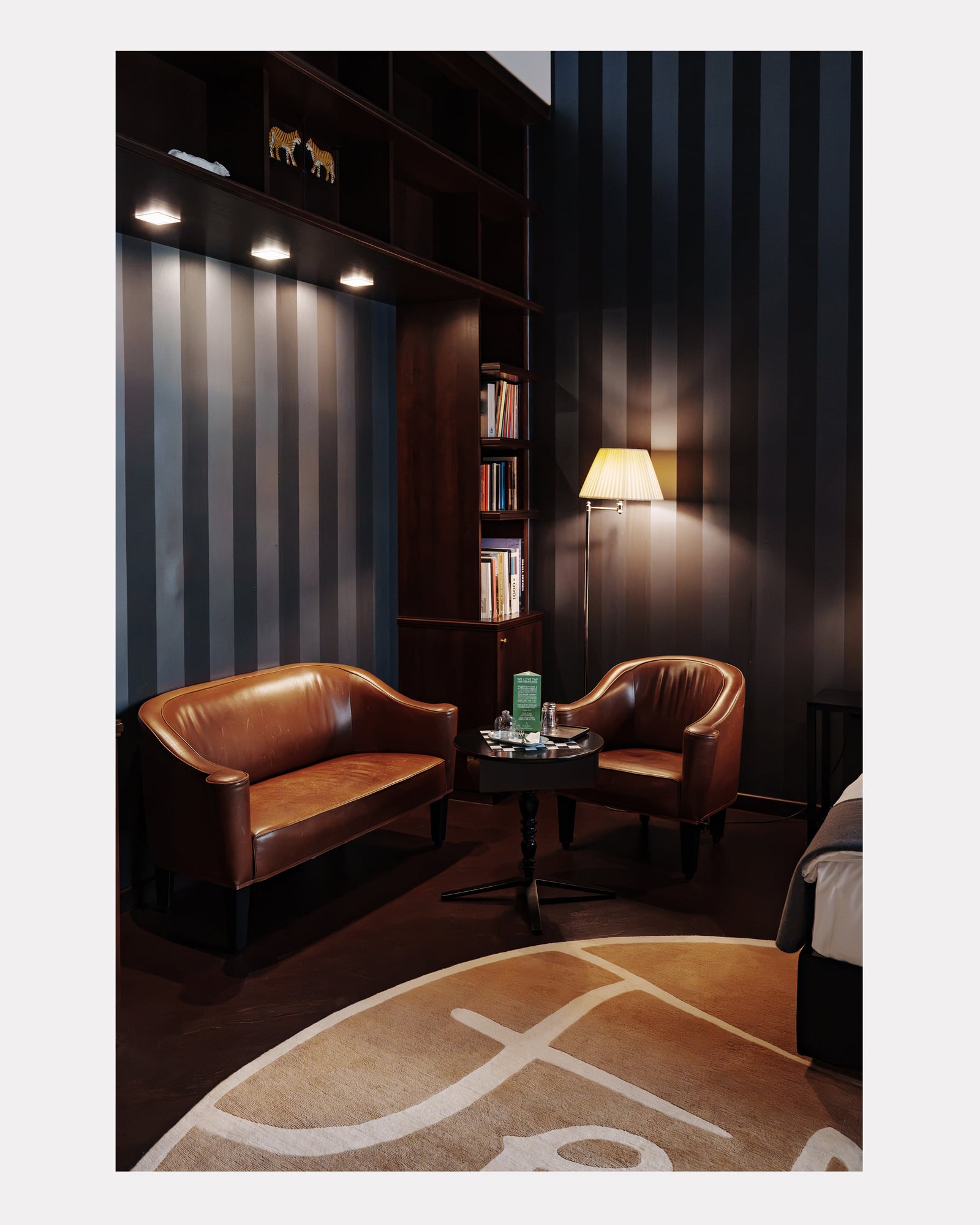 Coin salon avec canapé et fauteuils en cuir, murs rayés et bibliothèque, hôtel Altstadt Vienna
