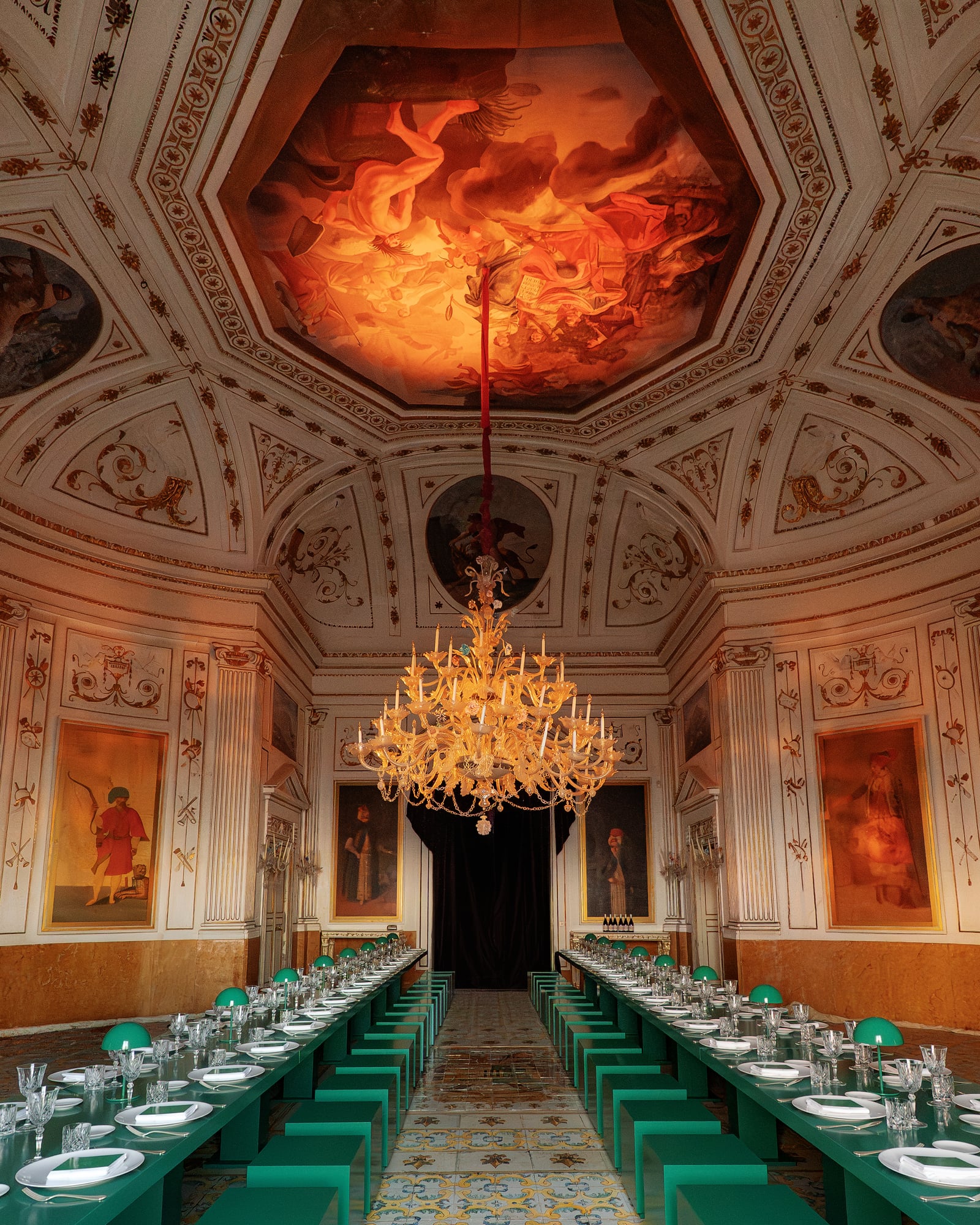 Salon au plafond peint rouge et lustre doré, longues tables vertes dressées pour un dîner de gala à Palerme