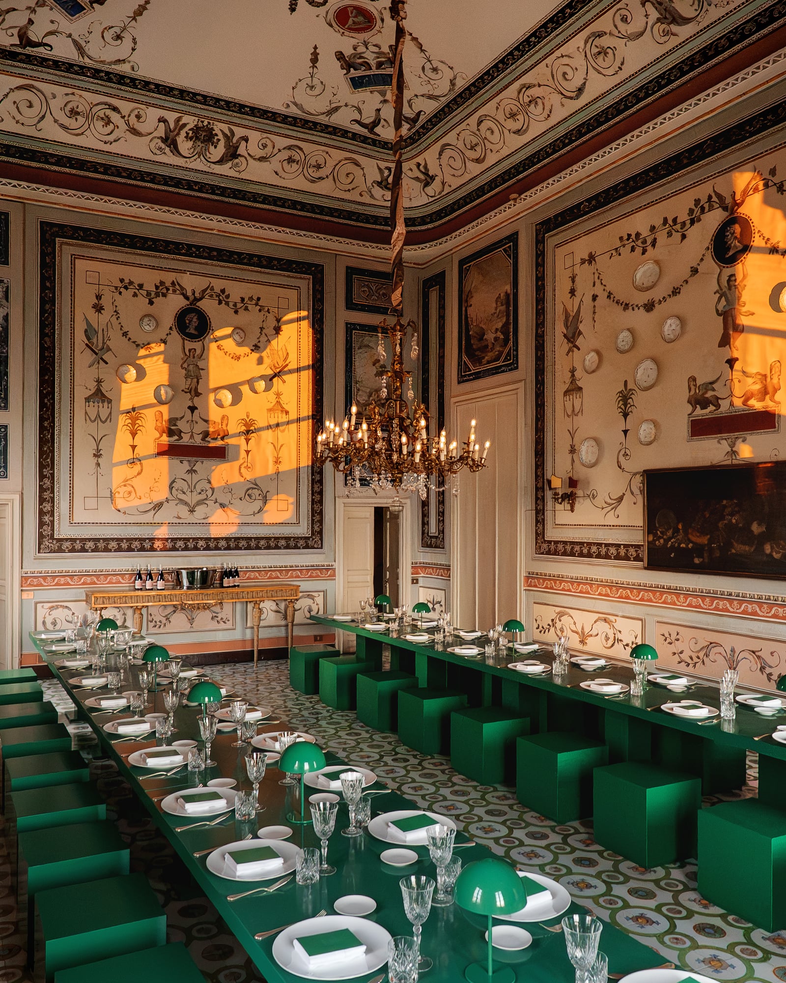 Salle aux murs ornés d'assiettes, lustre et tables vertes en perspective, dîner de gala à Palerme