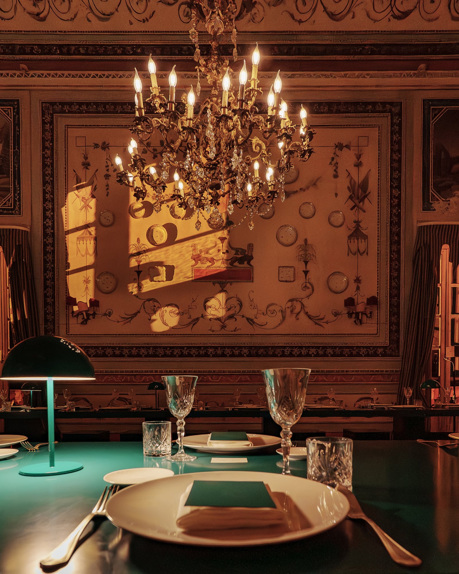 Lustre à bougies, lampe verte et assiette dressée devant un mur décoré, dîner de gala à Palerme